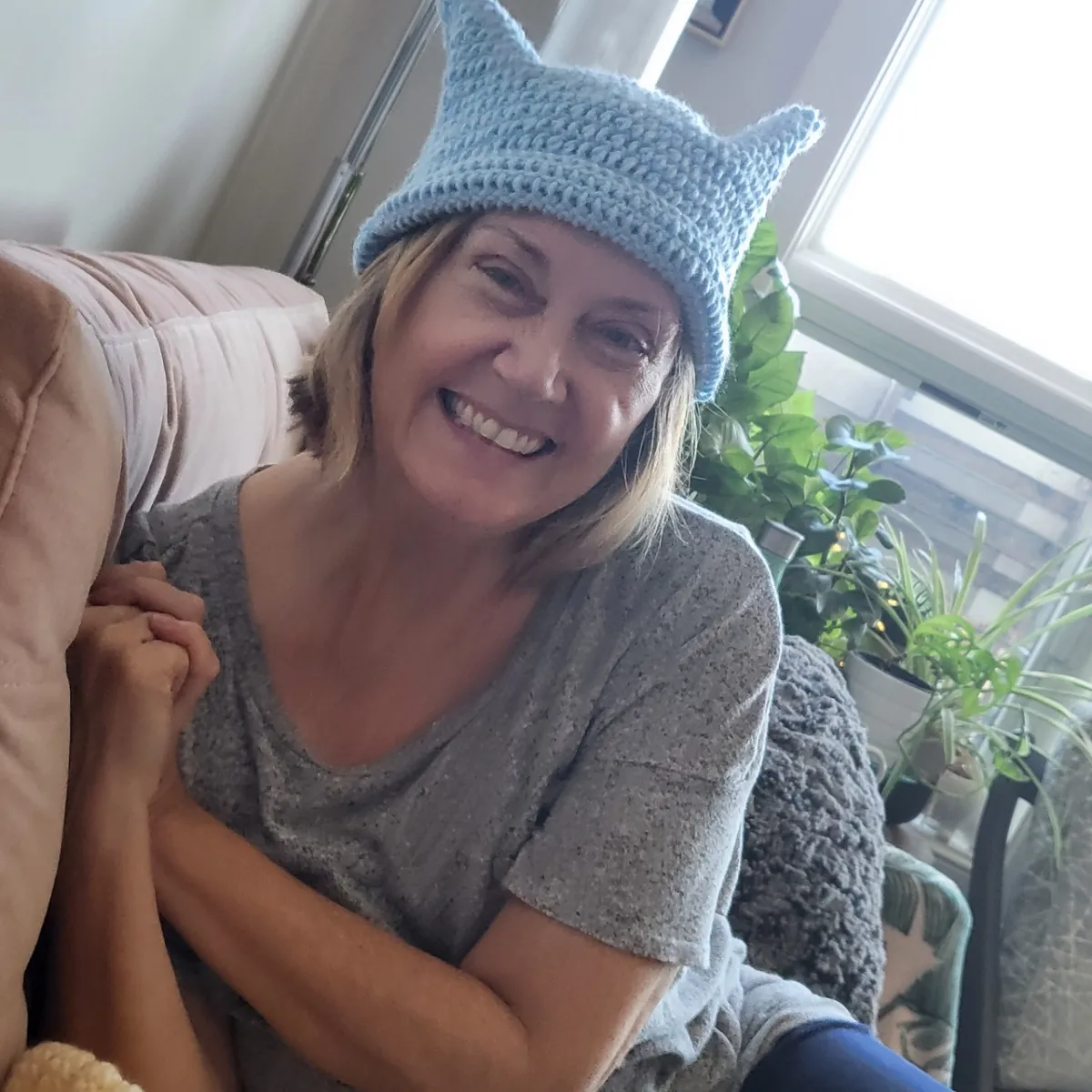 Deborah relaxing at home. She's got a big smile and is wearing a cute crocheted hat.