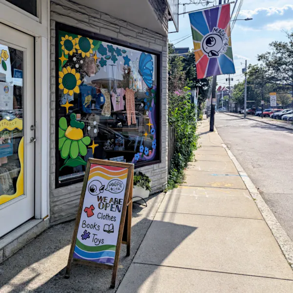View outside the store, with welcoming 'Open' sign and colorful flag with rainbow and cartoon magpie